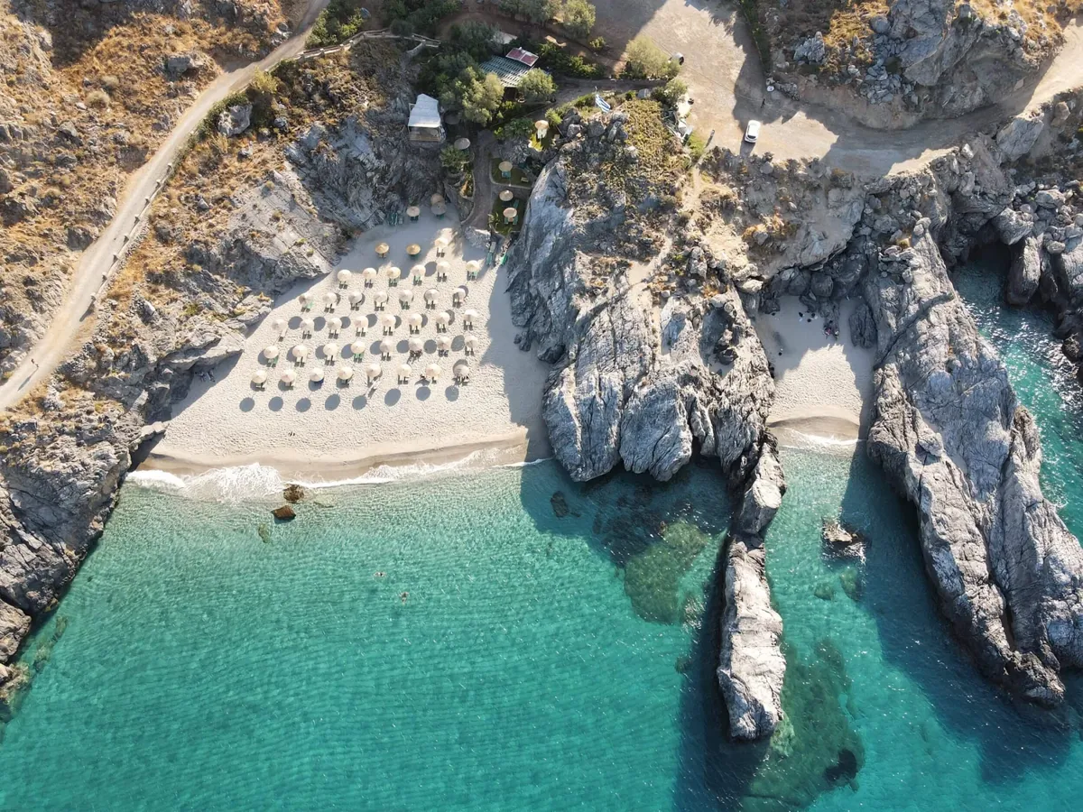 From above: the small sandy cove of Ammoudaki between white rocks, with clear turquoise water