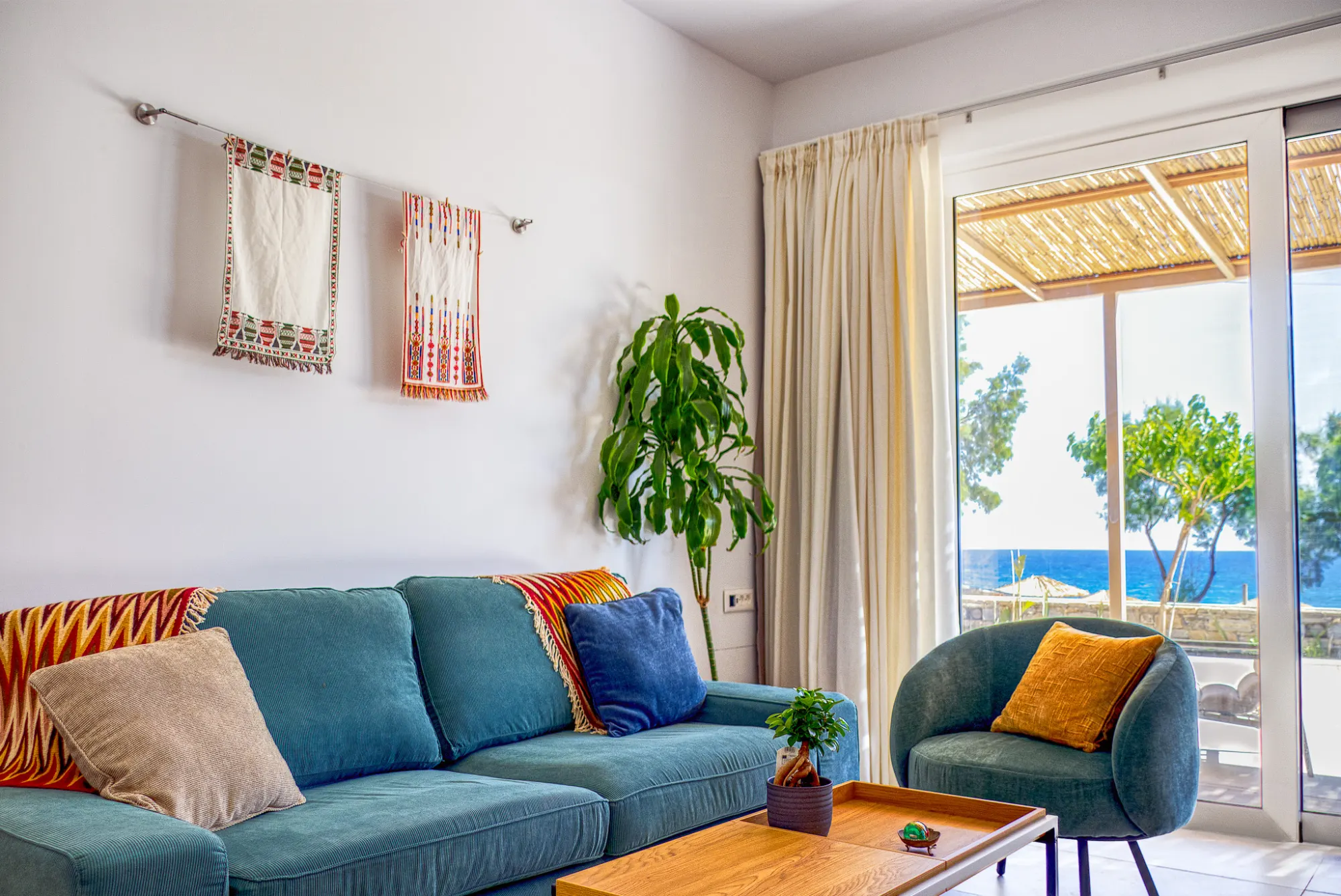 The apartment sitting room with woven Cretan textiles and the sea visible beyond the terrace