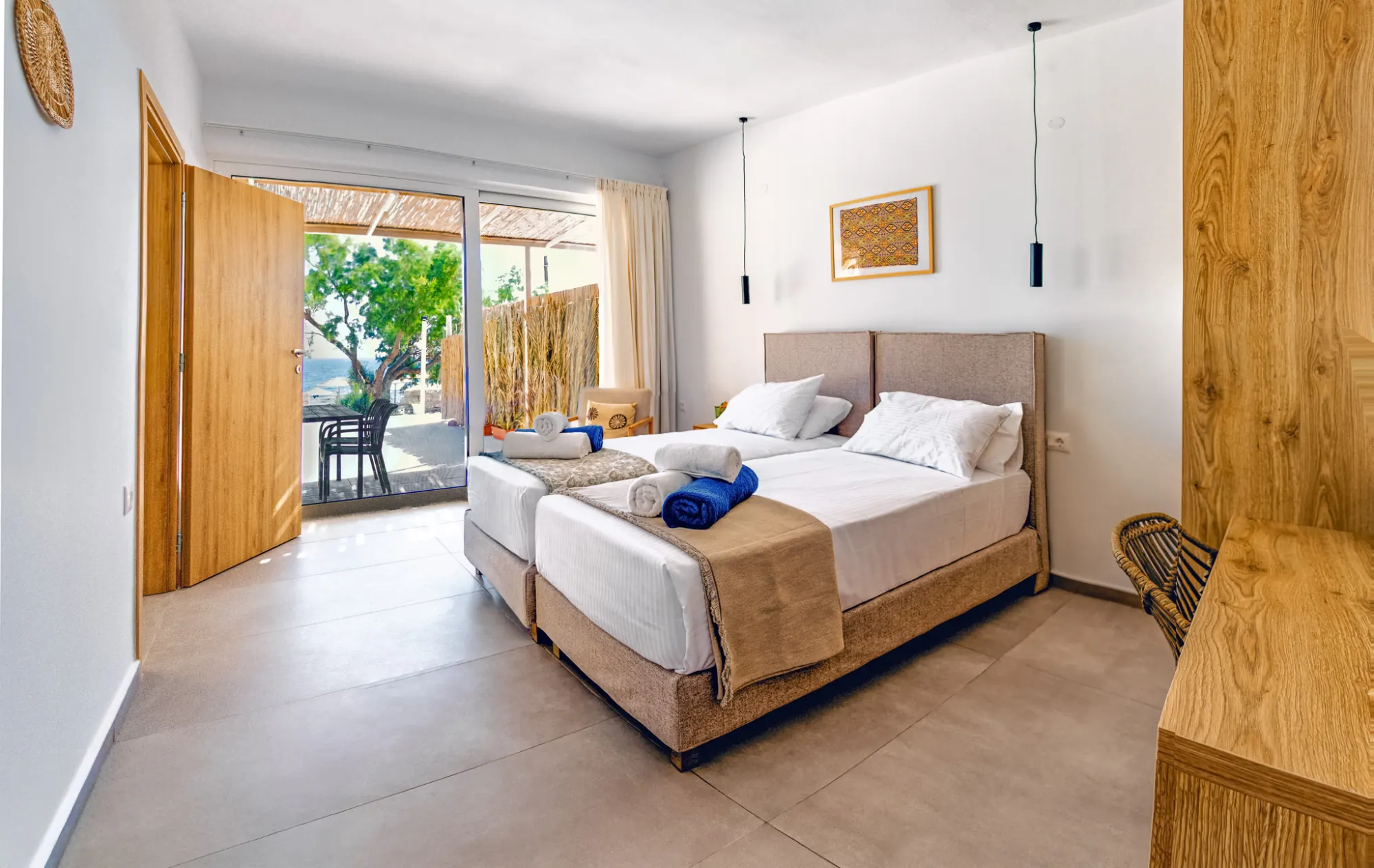 Bedroom with twin beds and rolled beach towels, its wooden door open to the terrace, the tamarisk tree and the beach beyond