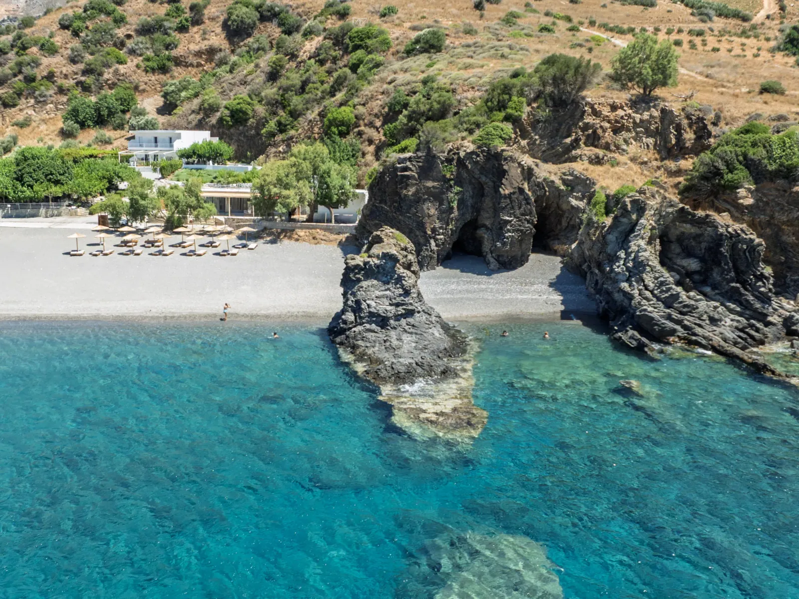 The rock arch and caves in clear turquoise water off Korakas, with the beach and the hills behind