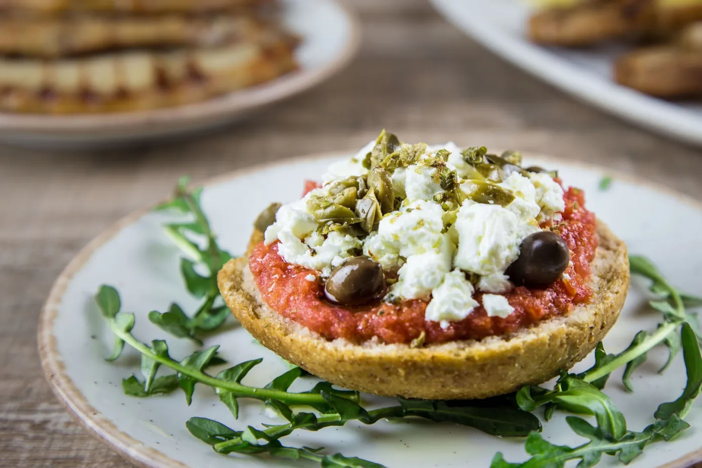 Dakos: a Cretan barley rusk topped with tomato, soft white cheese, capers and olives, on a bed of rocket