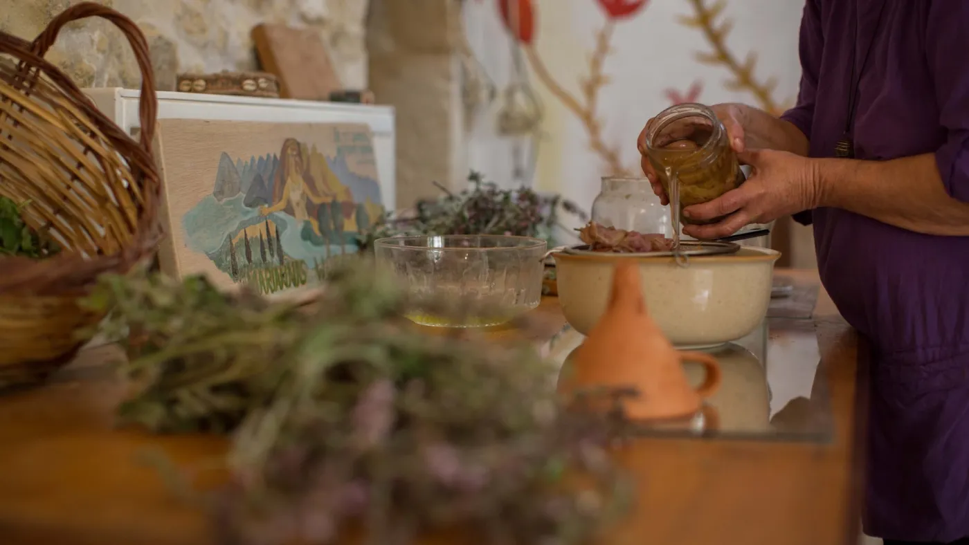 Hands jarring wild mountain herbs gathered from the hills, baskets of greens on the table