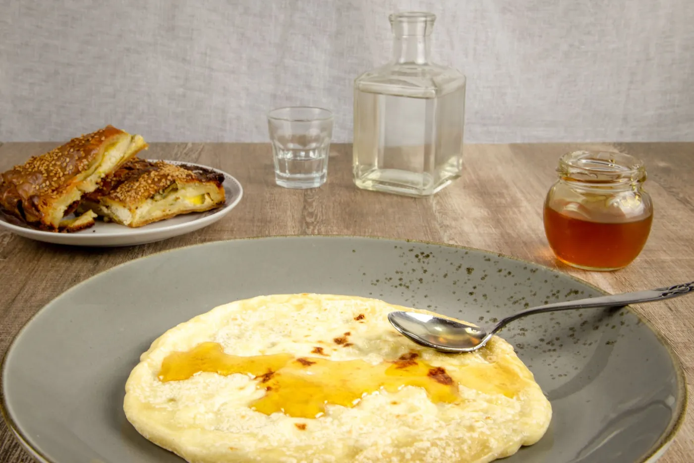 Sfakian pie drizzled with honey, a plate of sesame cheese pie behind it, and a carafe of raki