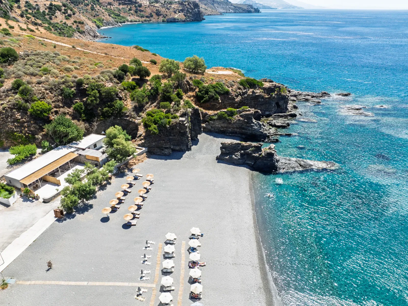 Korakas beach and the coast to the east: the house at the end of the beach, umbrellas on the pebbles, cliffs and turquoise water