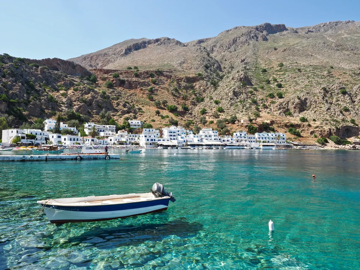 Loutro: white houses along a bay of clear green water under bare mountains, a small boat in front