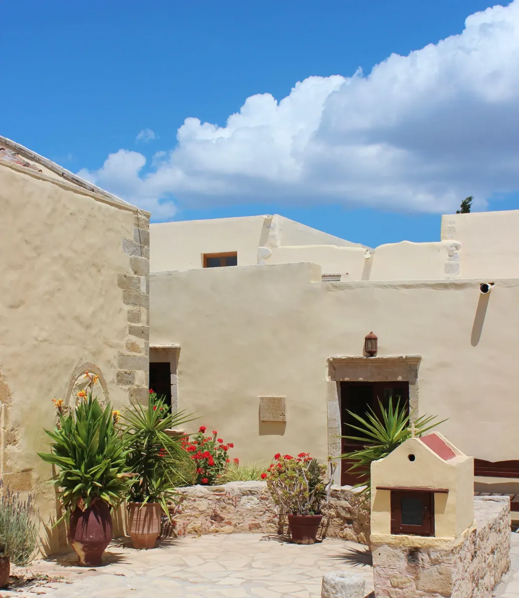 The stone courtyard of Preveli Monastery, with plants in pots under a blue sky