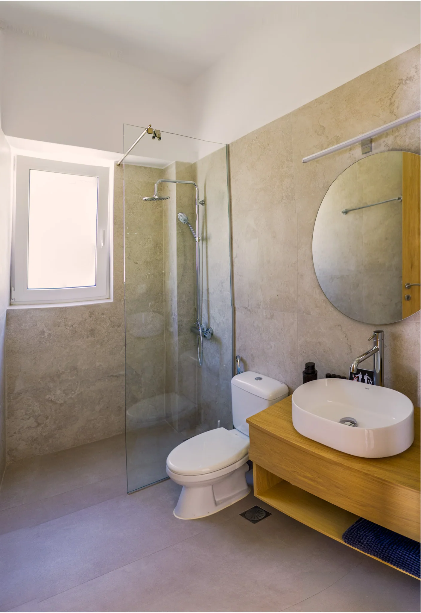 The studio bathroom with a walk-in rain shower, stone-finished walls, round mirror and oak vanity
