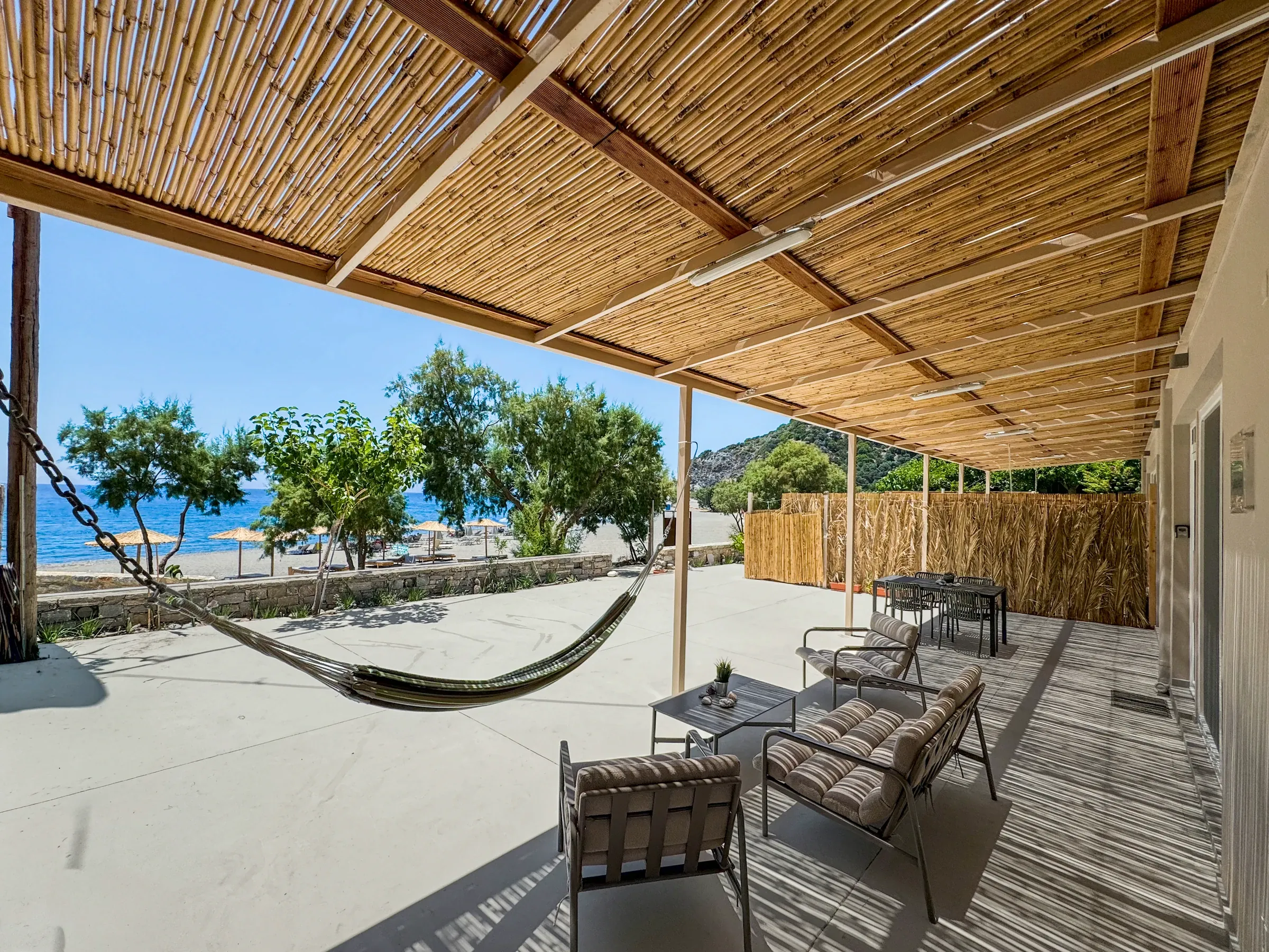 The shared terrace under its bamboo roof: a hammock and chairs, the trees, the beach and the sea beyond